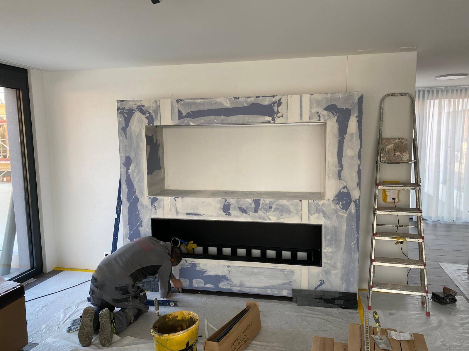 Artisan agenouille posant l'habillage sur mesure d'une cheminee moderne, niveau a bulle en main