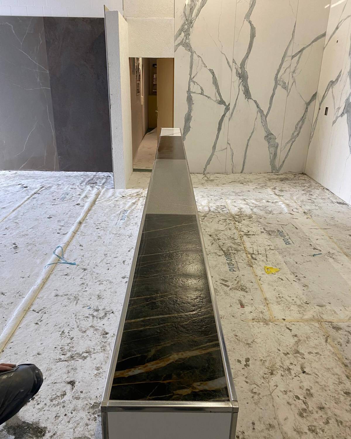 Detail showroom marbre : banc marbre noir veine devant mur marbre blanc veine gris