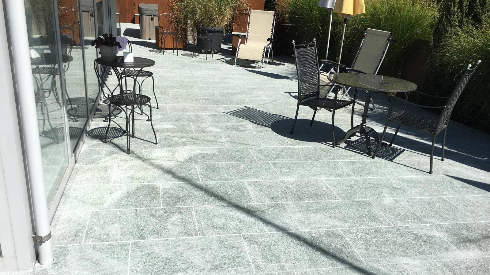 Terrasse en pierre grand format amenagee avec mobilier de jardin et brise-vue en acier corten