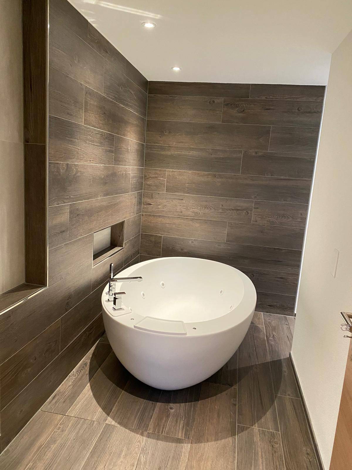 Salle de bain avec baignoire ilot ovale, double vasque suspendue et carrelage grand format effet bois