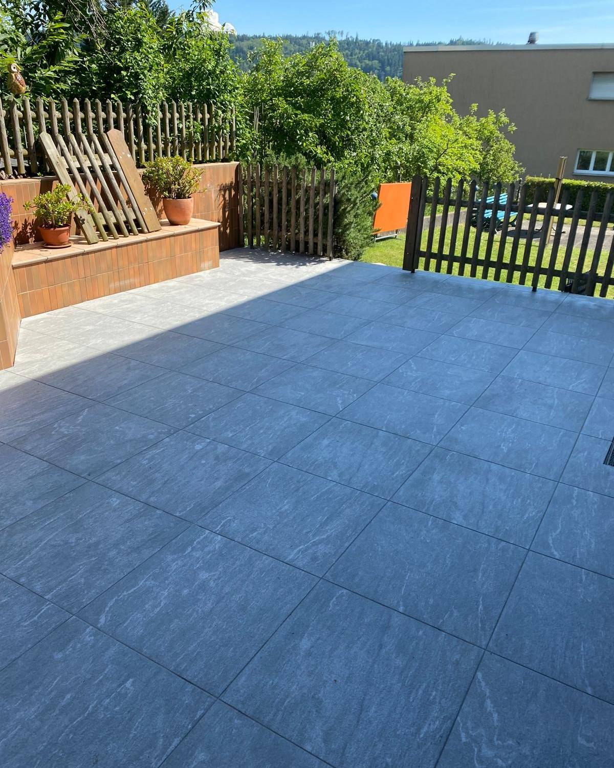 Terrasse carrelee gris clair integree dans un jardin arbore